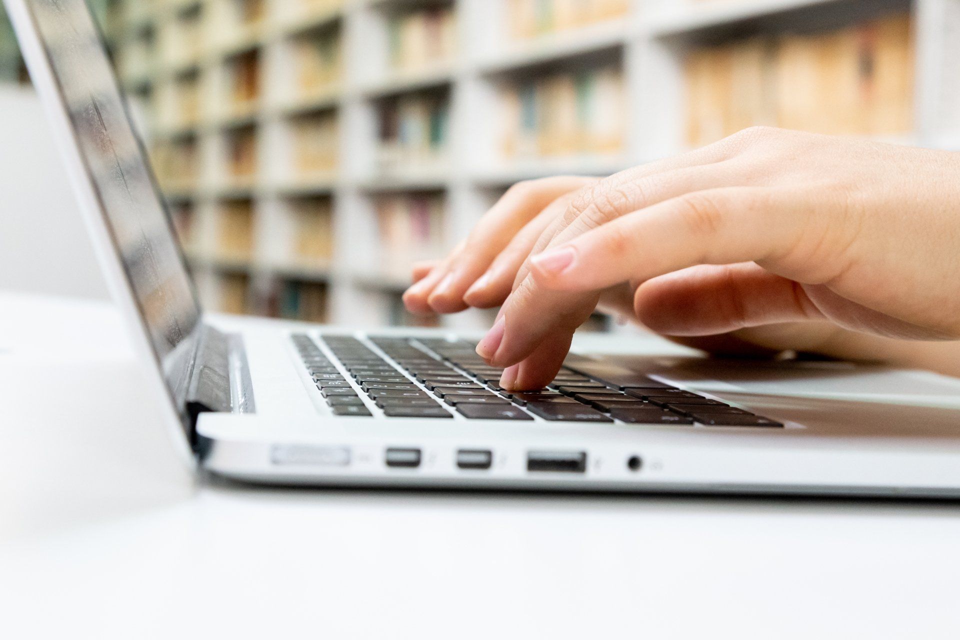 A Virtual Assistant is typing on a laptop computer in a library.