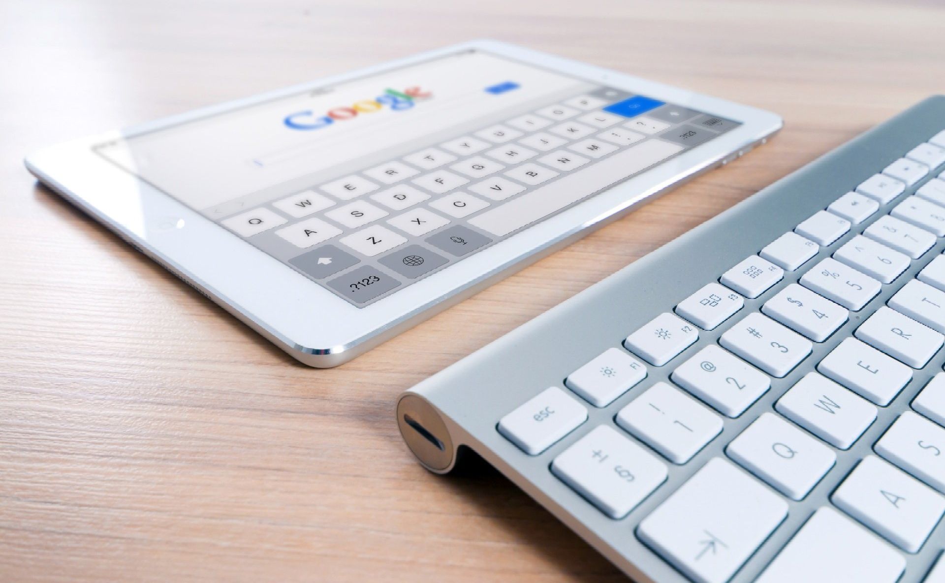 A tablet and a keyboard are on a wooden table.