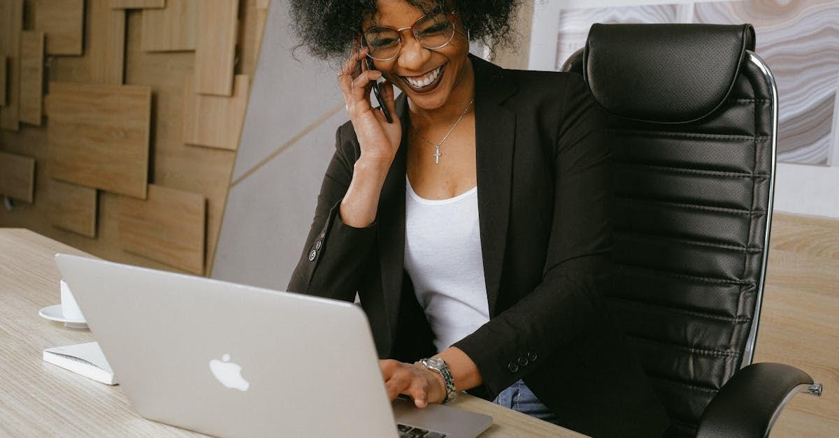 A Virtual Assistant is sitting at a desk talking on a cell phone while using a laptop computer.