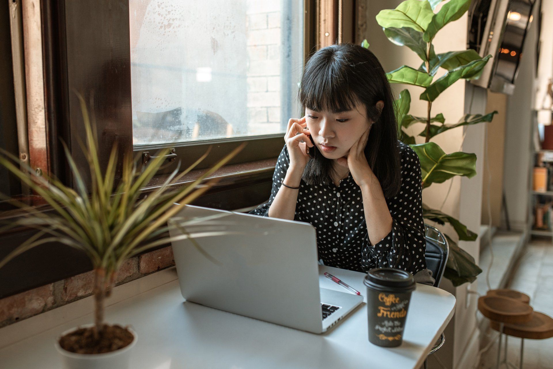 A Virtual Assistant is sitting at a desk using a laptop computer and talking on a cell phone.