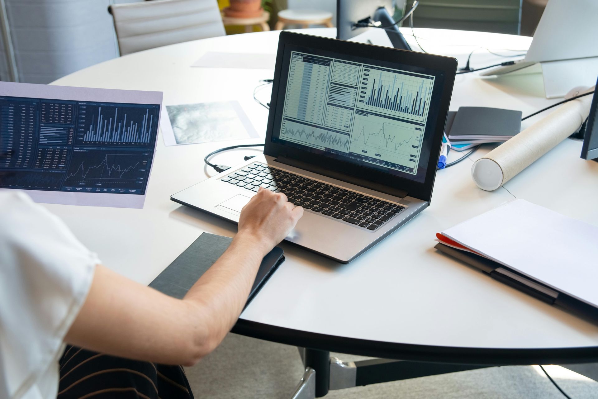 Person using laptop, possibly analyzing data displayed on screen, sitting at a round white table.