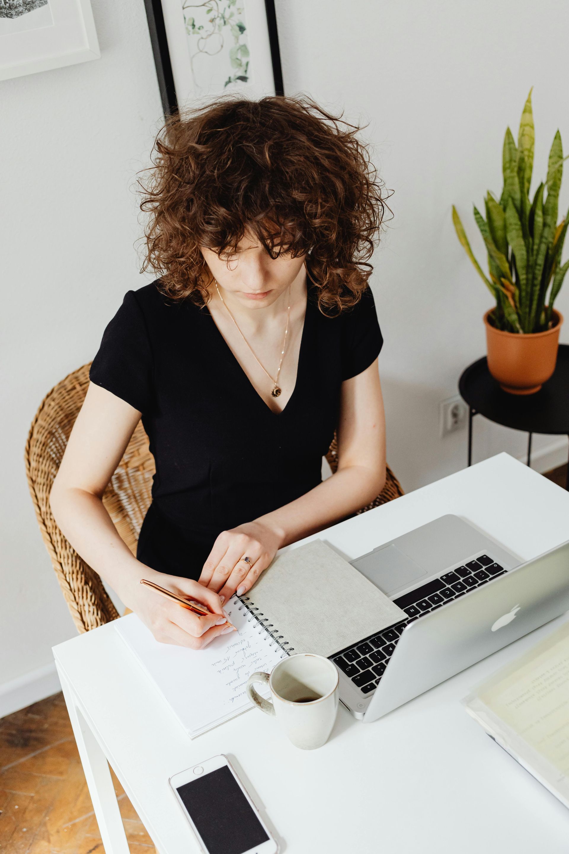 A woman is sitting at a desk with a laptop and writing in a notebook.