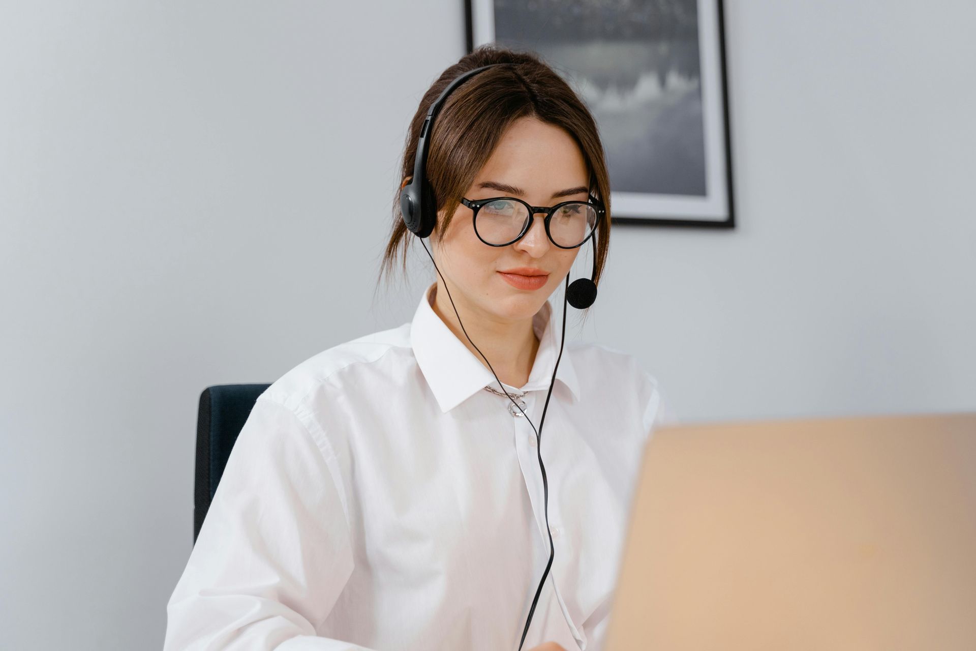 A woman wearing a headset and glasses is sitting at a desk.