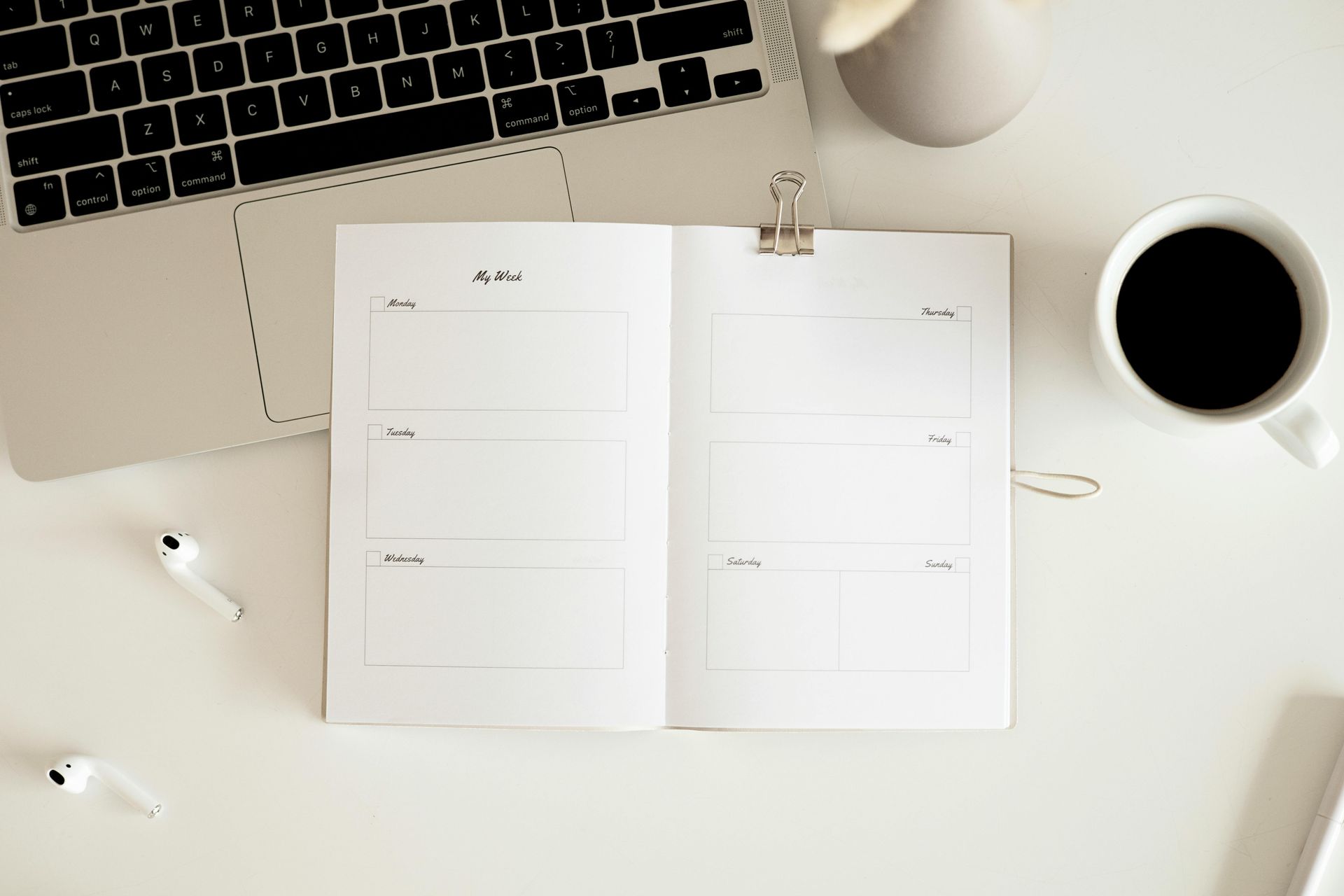 A notebook is open on a desk next to a laptop and a cup of coffee.