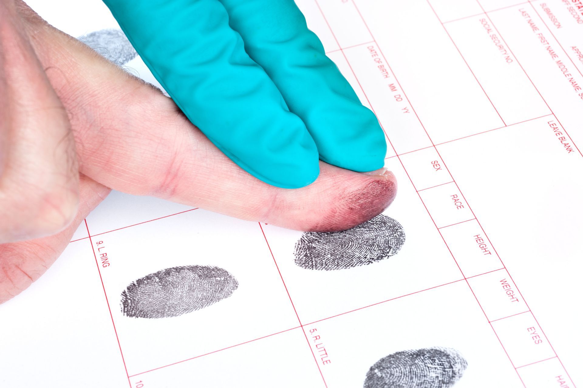 Finger applying ink to create a fingerprint on white paper; black ink and finger visible.