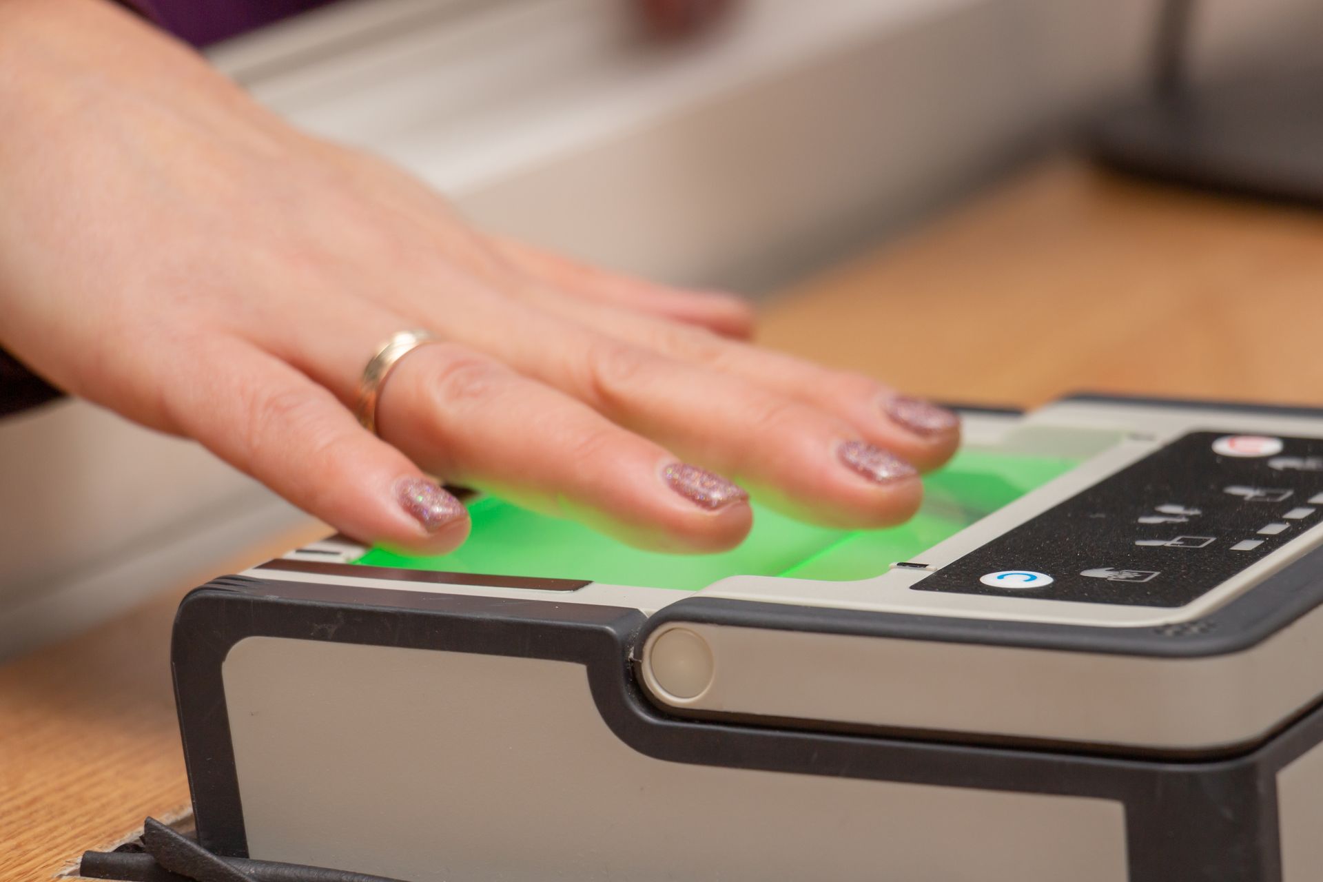 Person's hand on a fingerprint scanner, illuminated in green, possibly for identification or security.