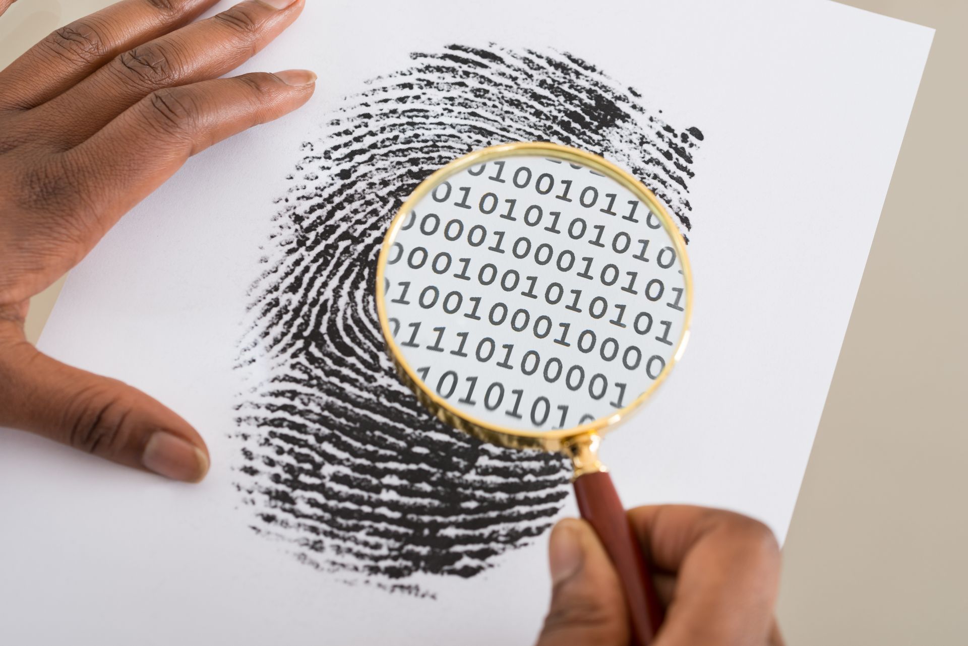 Close-up of a person's hands examining a fingerprint with a magnifying glass; binary code overlaid.