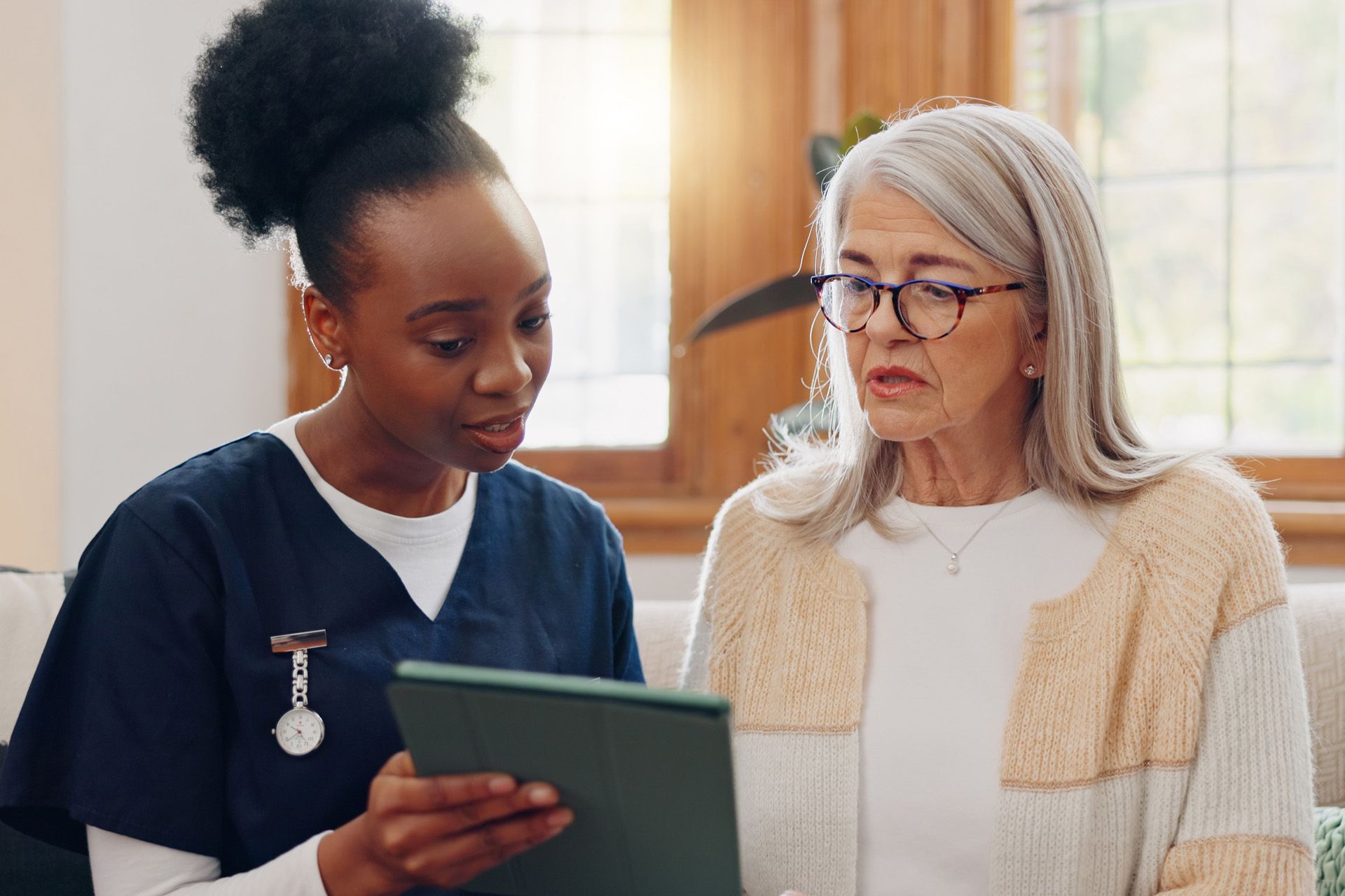 Nurse showing elderly patient on tablet indoors.