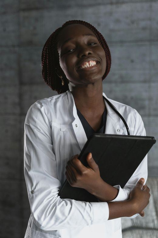 Woman with short hair, wearing a white shirt and apron, smiles in front of a plant.