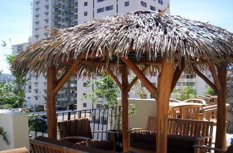A wooden gazebo with a thatched roof sits in front of a building