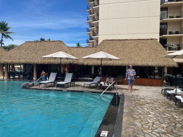 A man is standing next to a swimming pool with thatched roofs.
