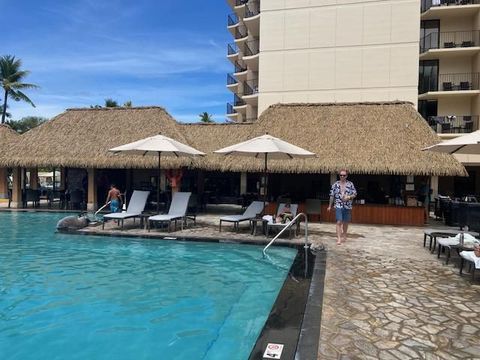 A man is standing next to a swimming pool with thatched roofs.