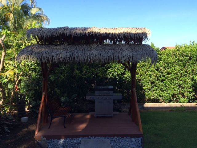 A gazebo with a thatched roof and a grill in the backyard.