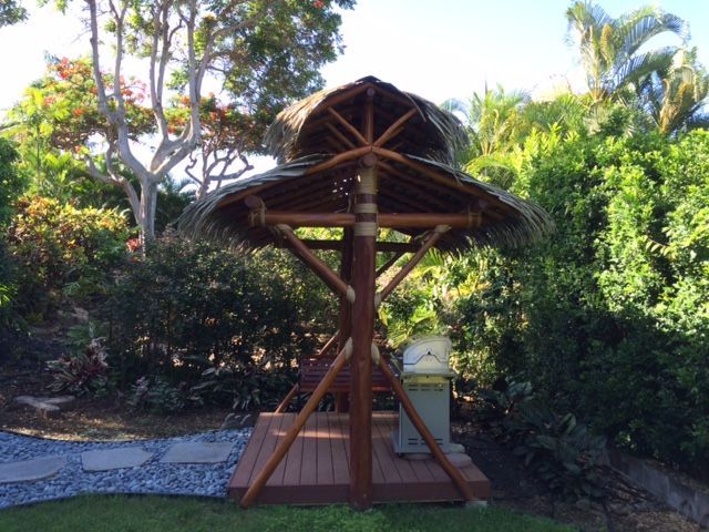 A wooden gazebo with a thatched roof in a garden