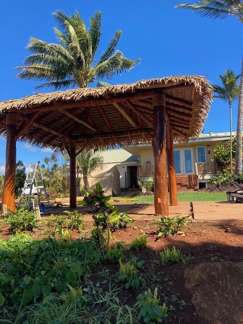 A thatched gazebo in front of a house with palm trees