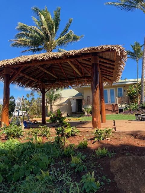 A thatched gazebo in front of a house with palm trees