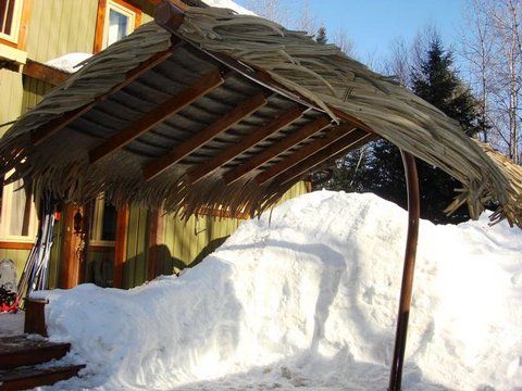 A thatched roof is covered in snow in front of a house