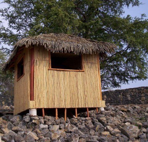 A small hut with a thatched roof sits on top of a pile of rocks