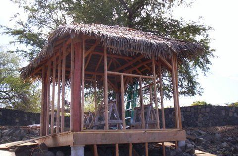 A wooden structure with a thatched roof is under construction