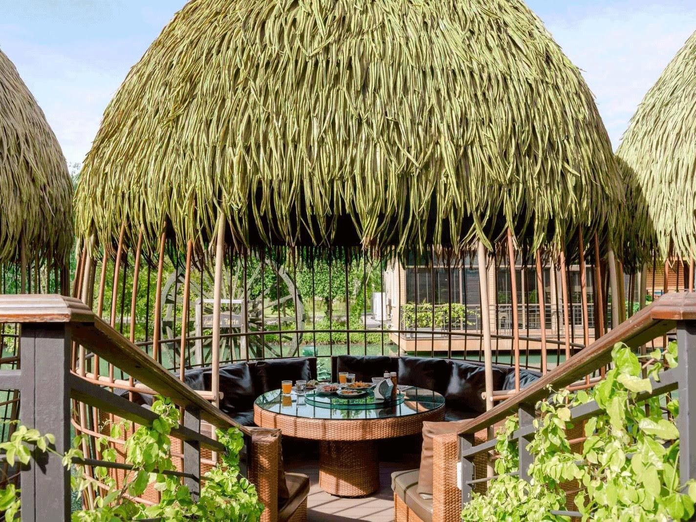 A gazebo with a table and chairs under a thatched roof.