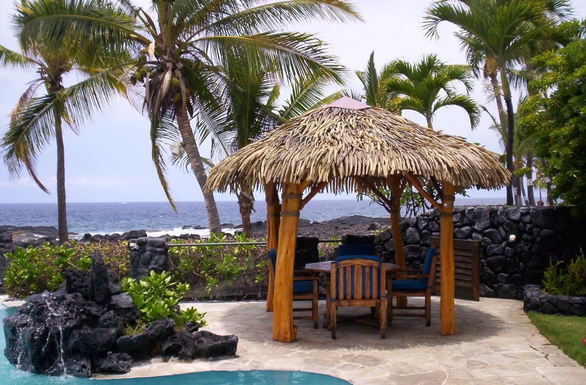 A gazebo with a thatched roof sits next to a pool