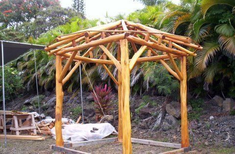 A wooden gazebo is being built in a yard with trees in the background.
