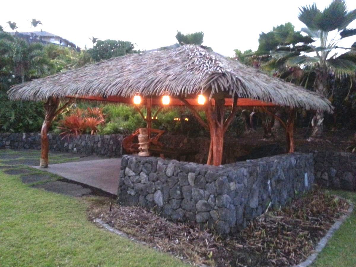 A gazebo with a thatched roof is in the middle of a lush green field.