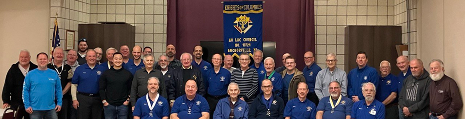 A large group of people posing for a photo indoors in front of a blue banner, wearing casual attire.