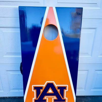 A blue and orange cornhole board with the letter a on it is sitting in front of a garage door.