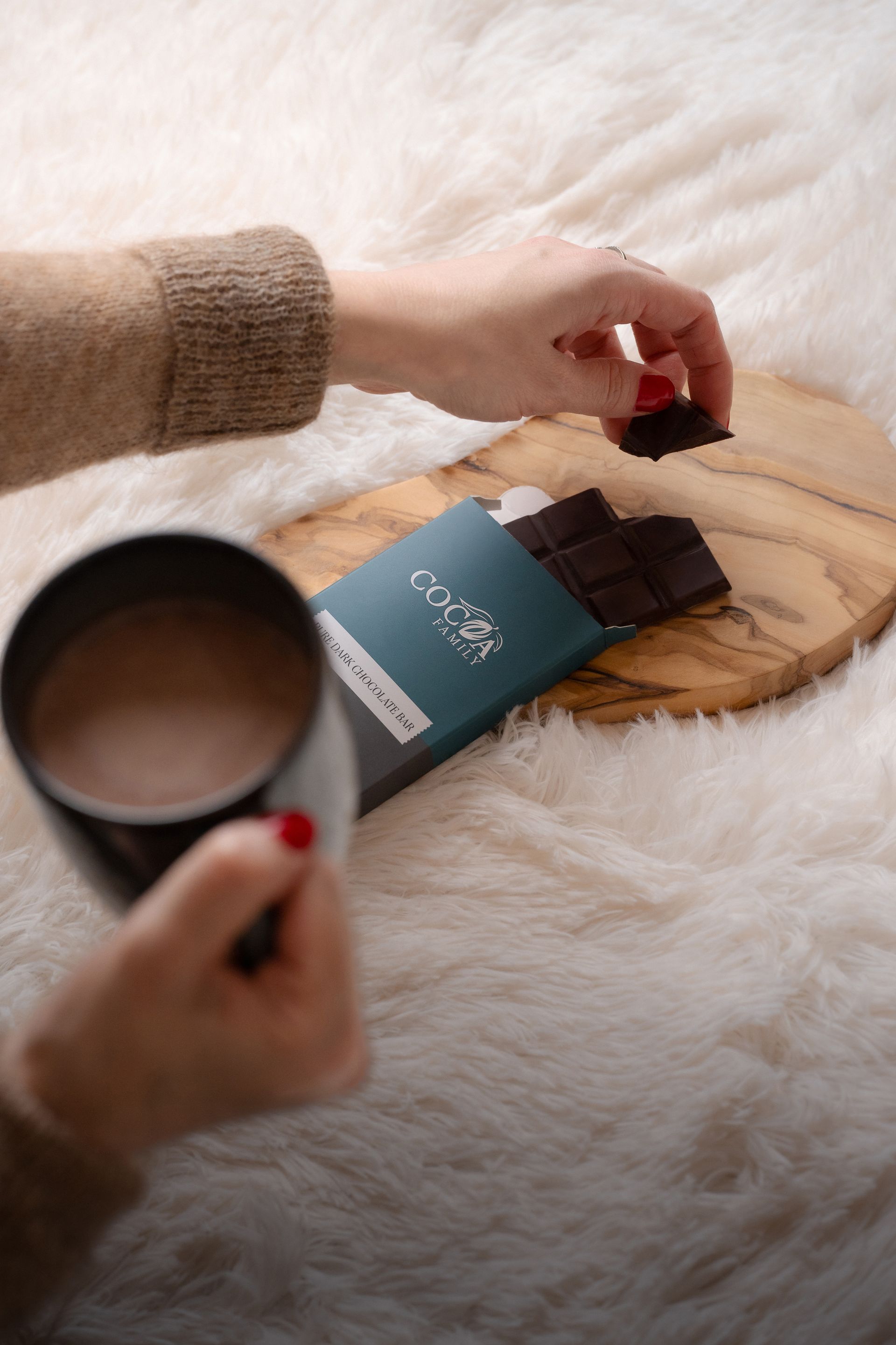 A person is holding a cup of hot chocolate and a bar of chocolate