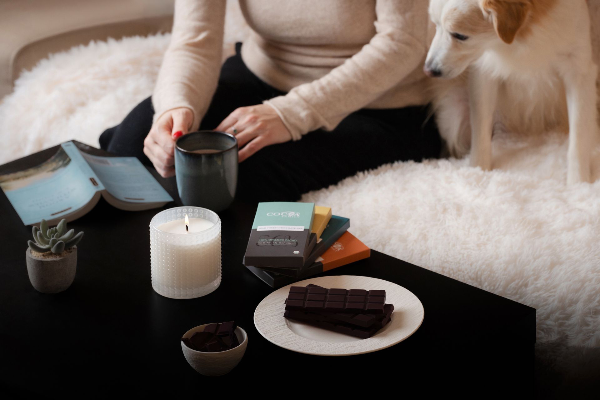 A woman sits on a couch with a dog and a cup of coffee