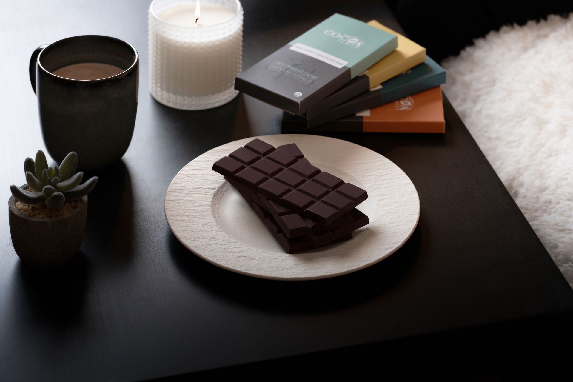 A plate of chocolate sits on a table next to a cup of coffee and a candle