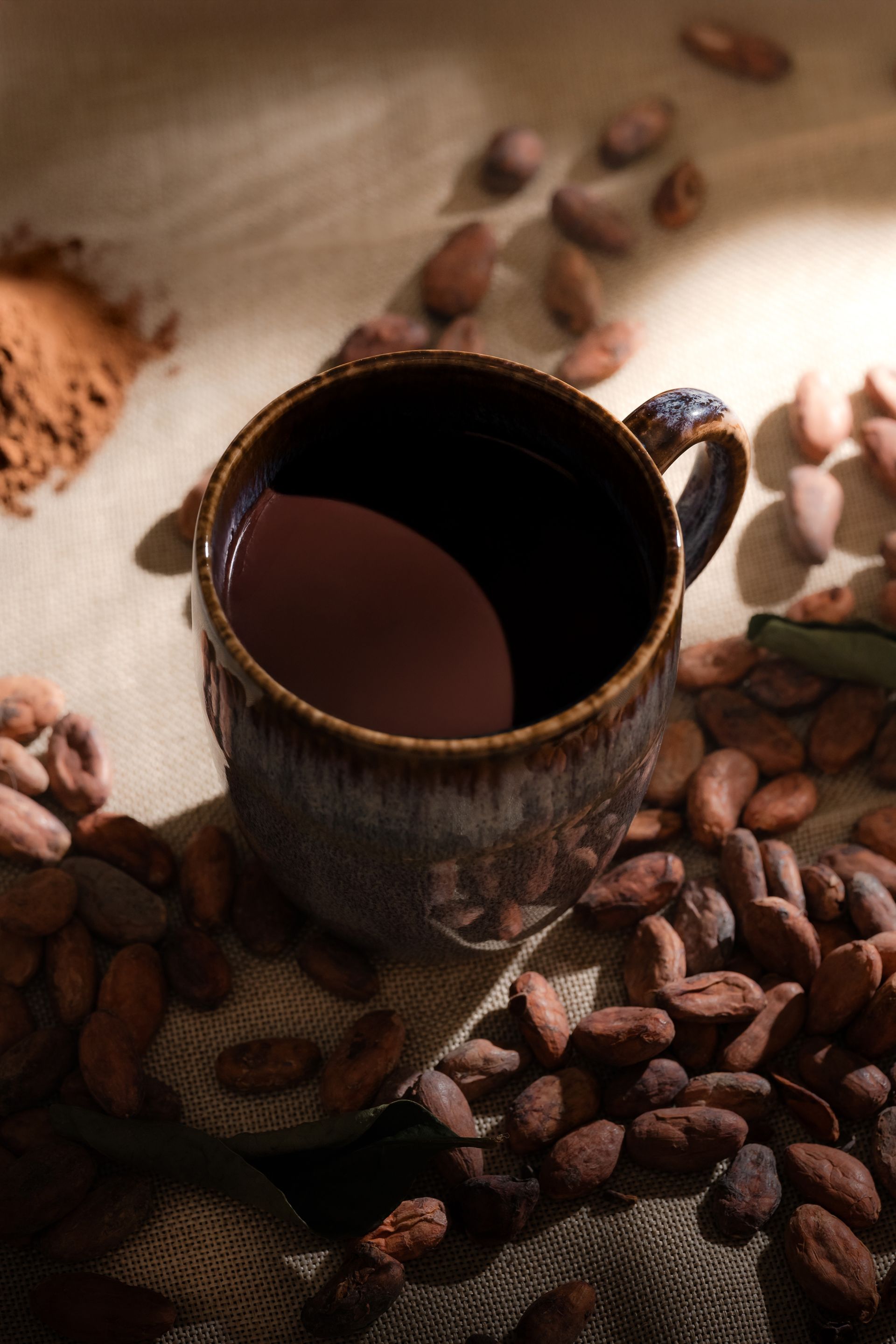 A cup of hot chocolate surrounded by cocoa beans