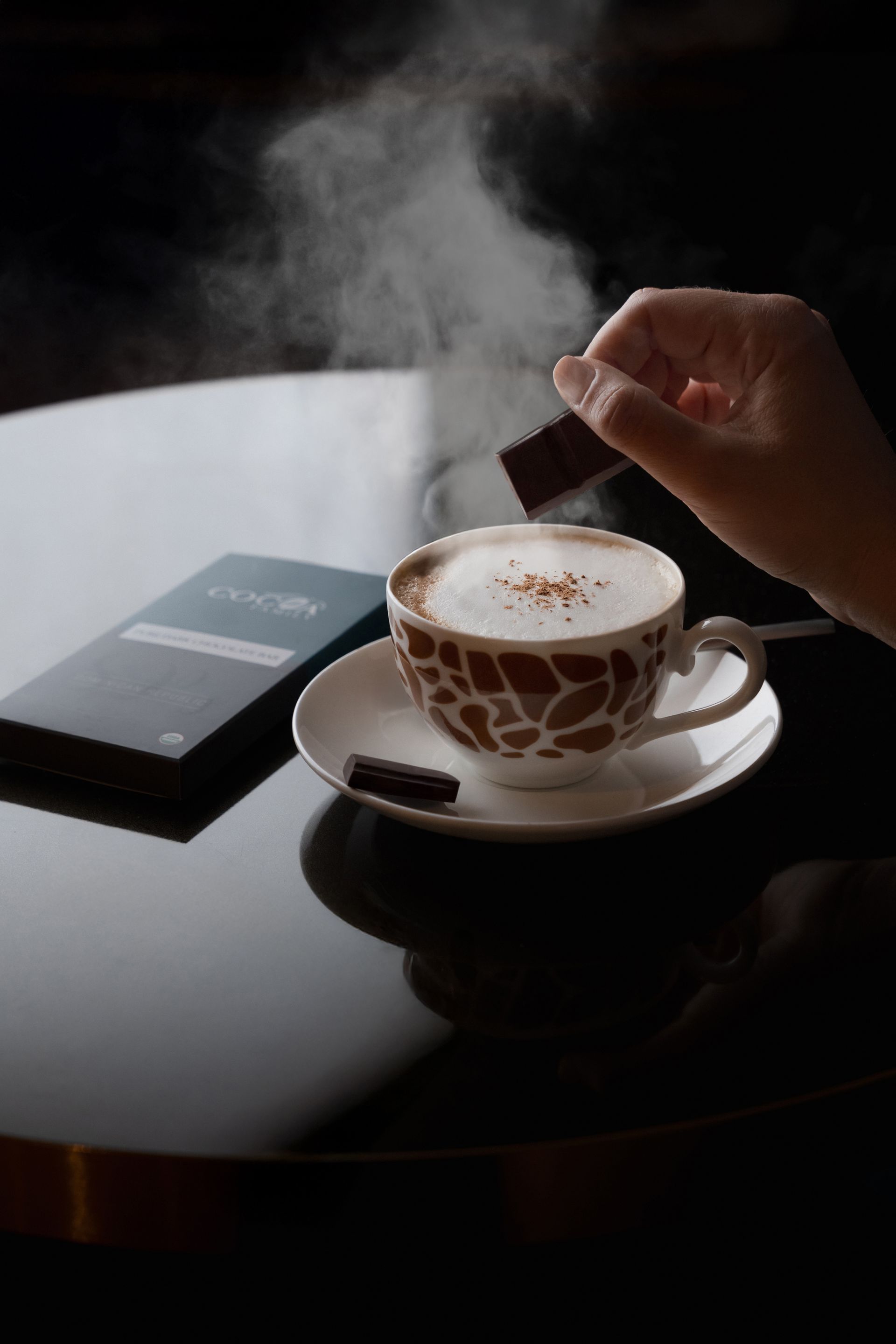 A person is dipping a piece of chocolate into a cup of coffee