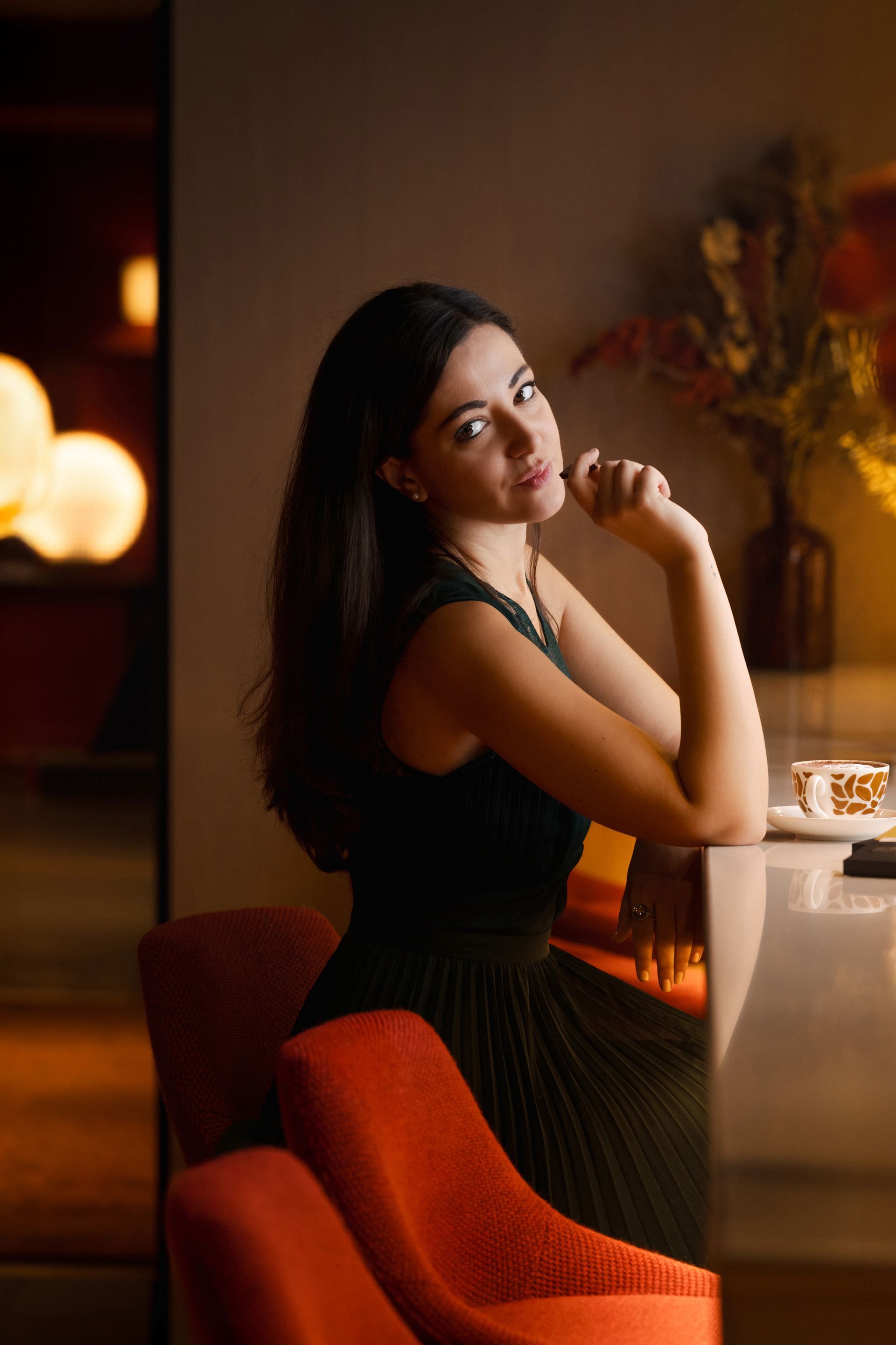 A woman in a black dress sits at a table with her hand on her chin