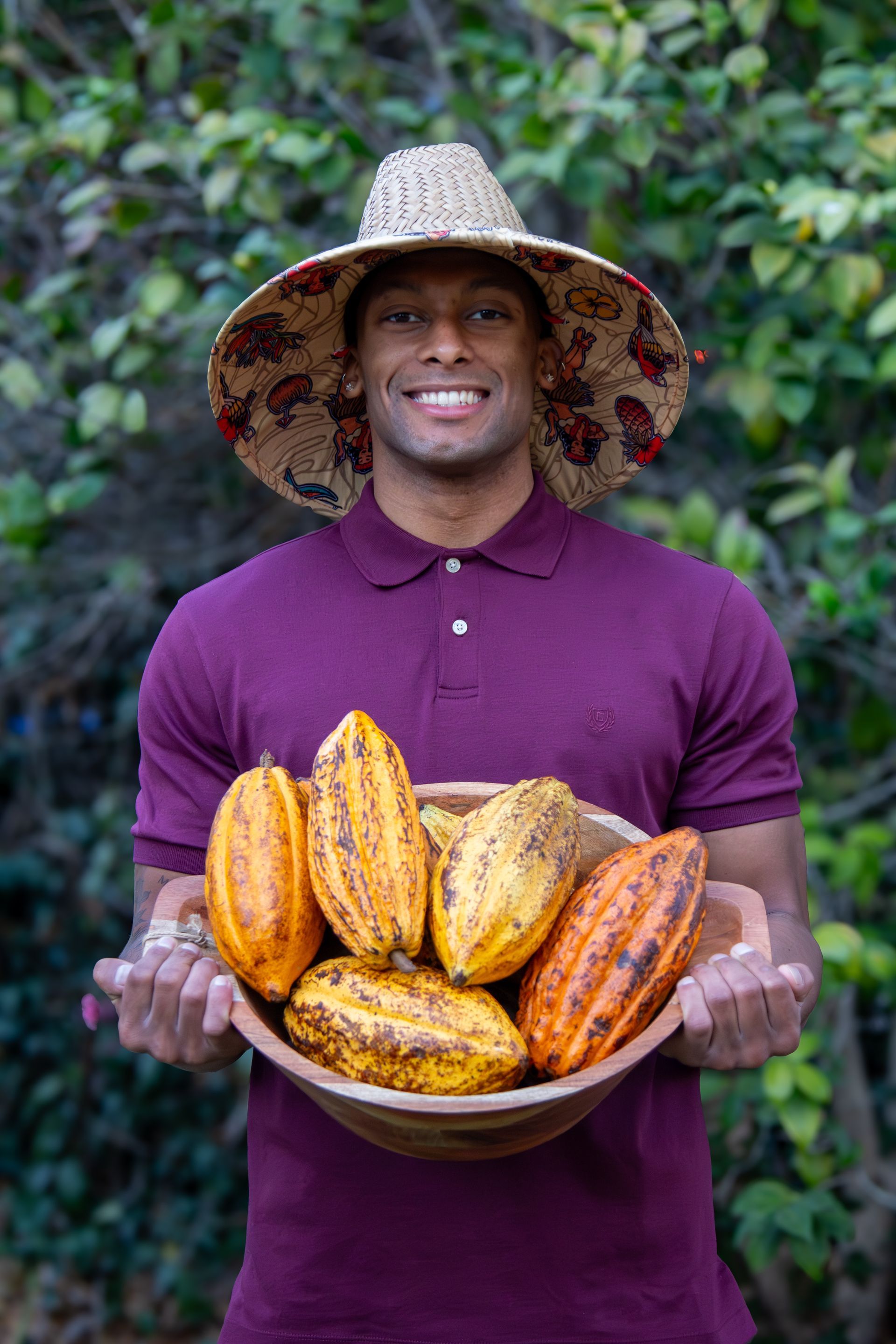 A man wearing a hat is holding a bowl of cocoa pods