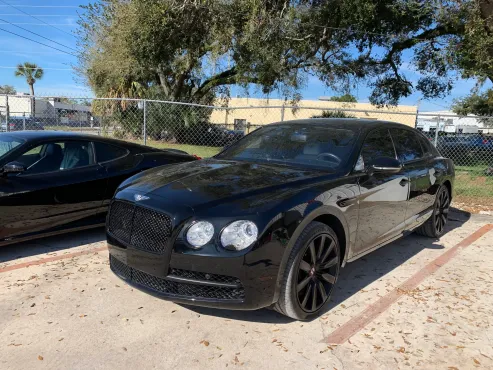 Black Bentley parked in a lot next to a black sports car on a sunny day.