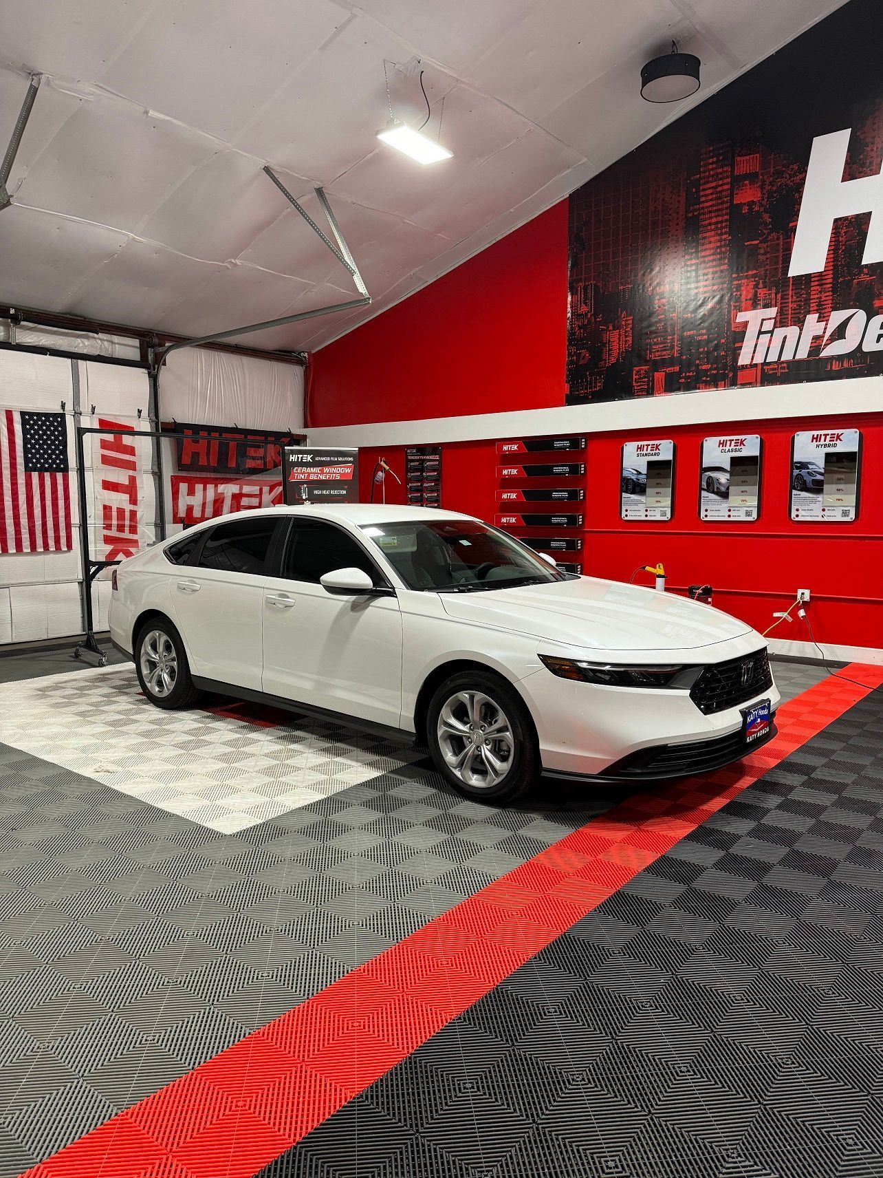 White sedan in a shop with red accents and tiled floor. American flag hangs on the left.