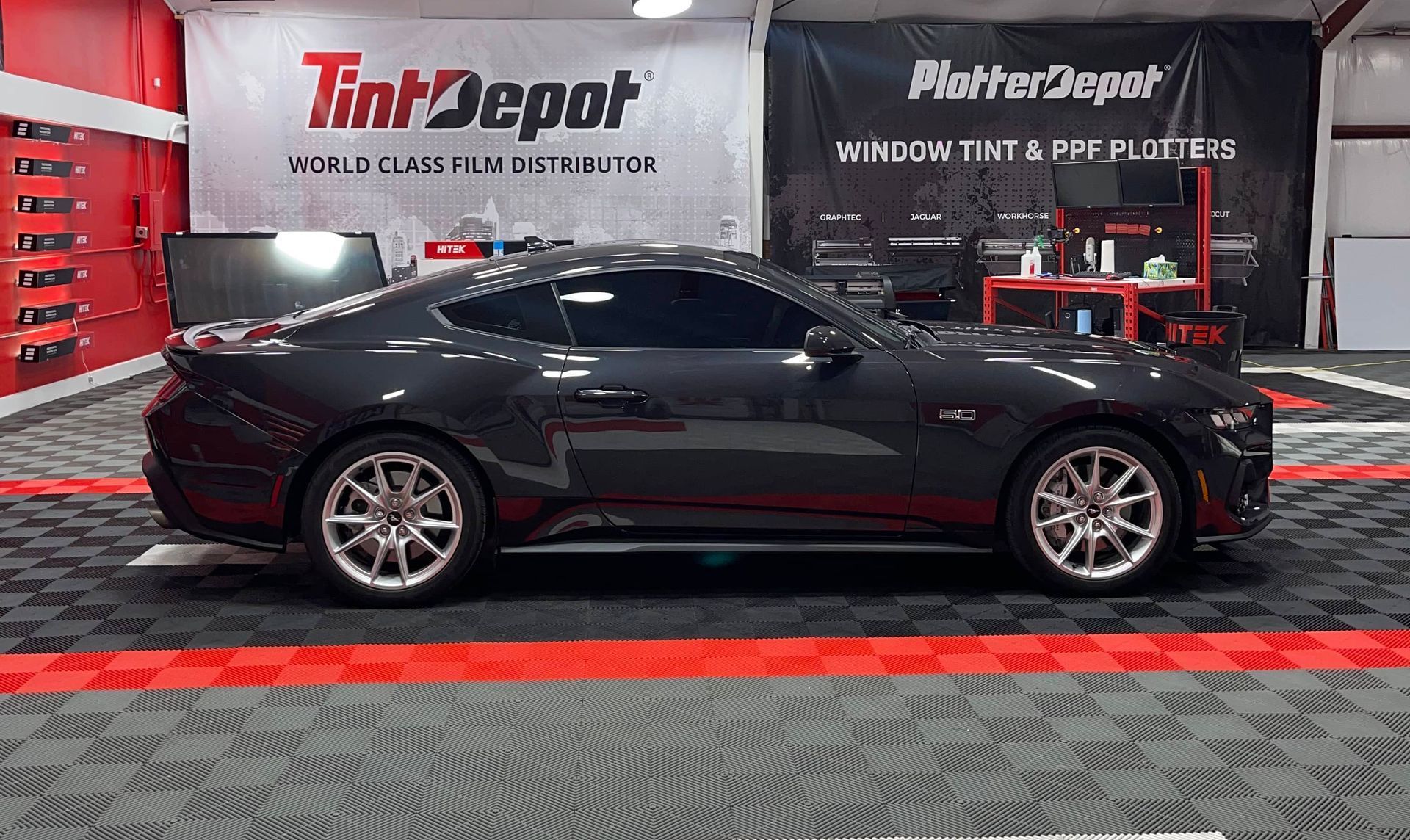 Dark gray sports car with tinted windows parked in a shop with flooring tiles.
