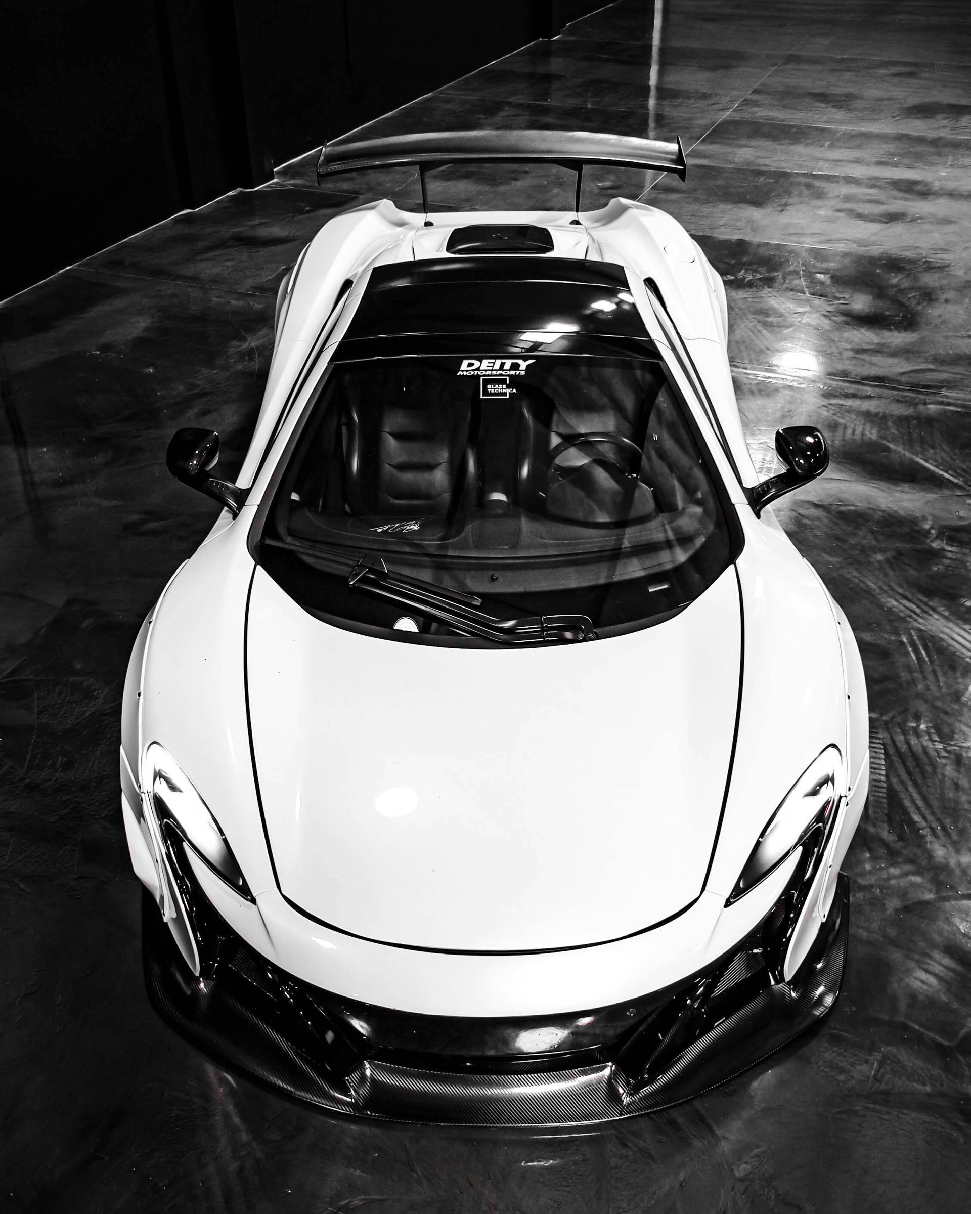 White McLaren sports car, top-down view, black accents, parked on a reflective surface.