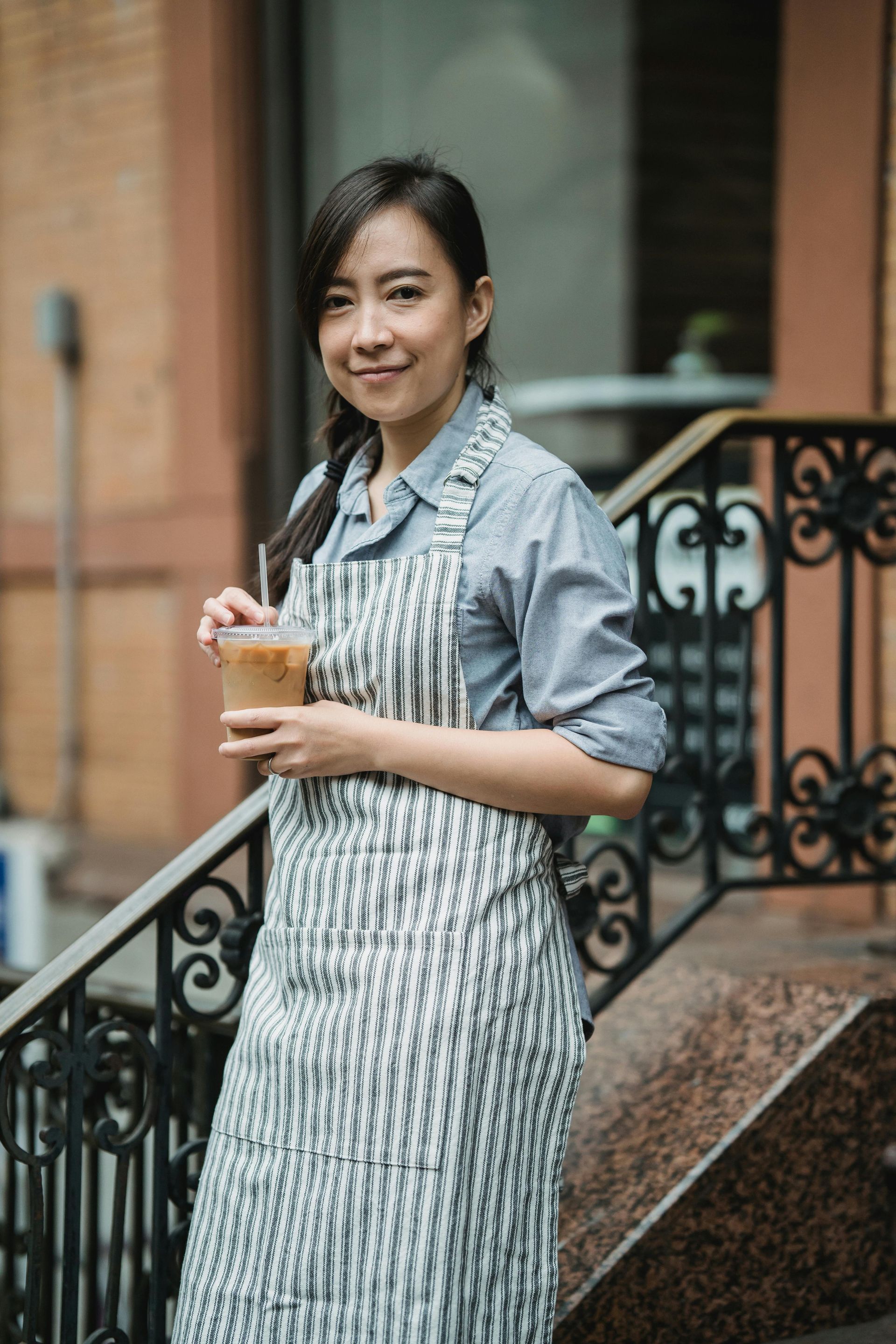 A woman in an apron is standing on a set of stairs holding a cup of coffee.