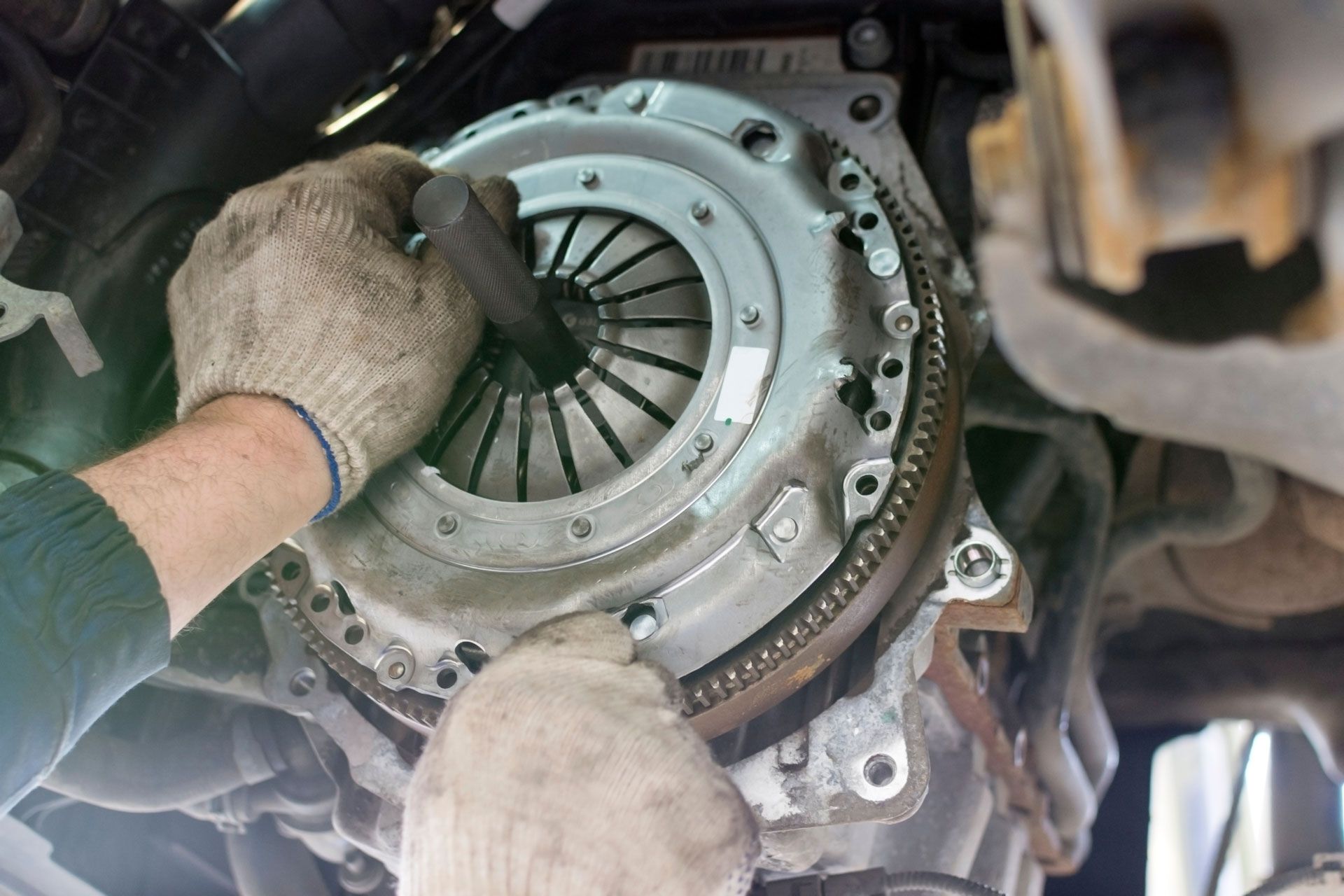 Mechanic removing a car clutch assembly under the vehicle with gloved hands