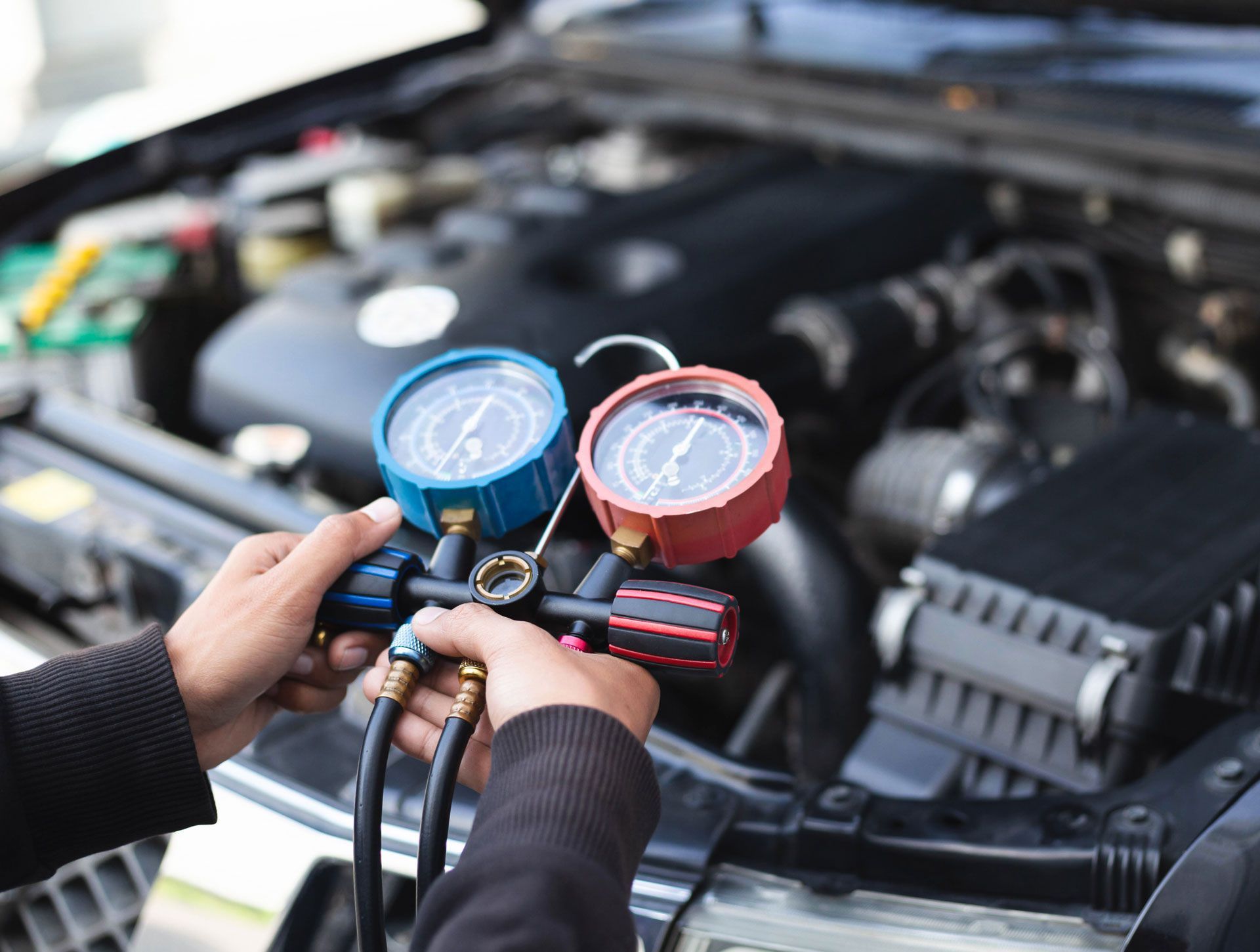 Mechanic holding blue and red gauges while checking car air conditioning system under the hood