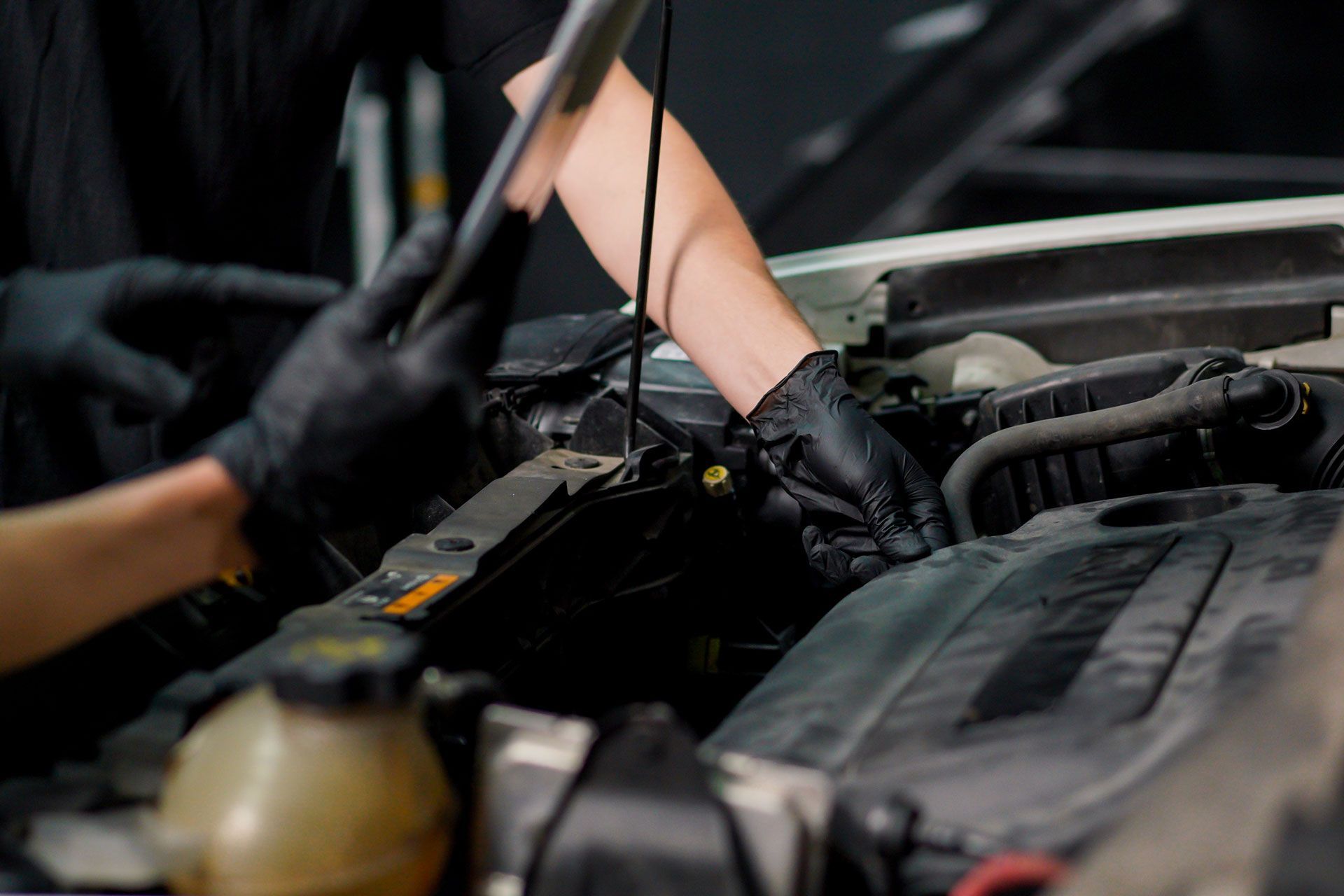 Gloved mechanic inspecting a car engine bay with tools nearby
