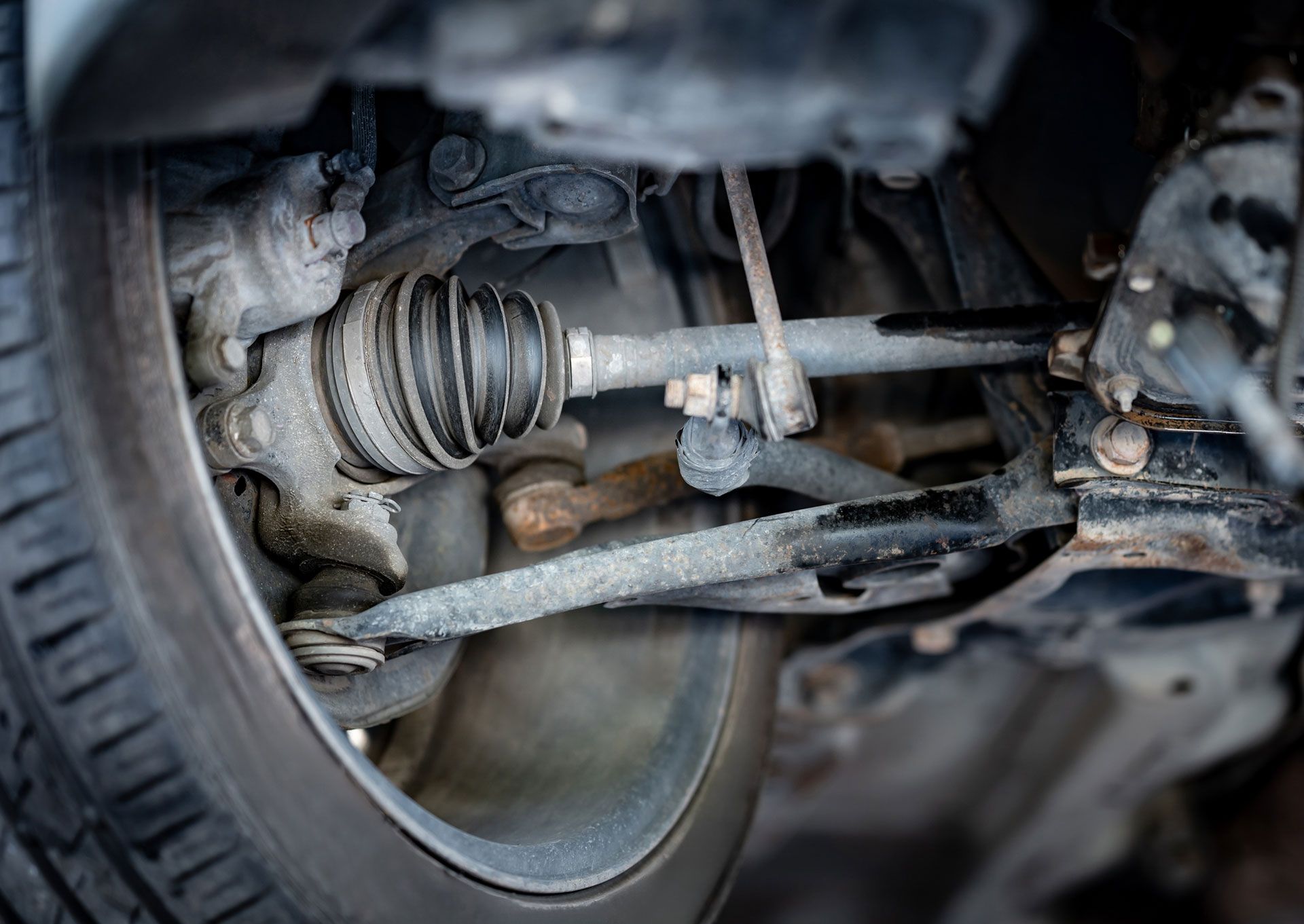 Close-up of a car’s exposed suspension and steering components, with a wheel and axle visible.