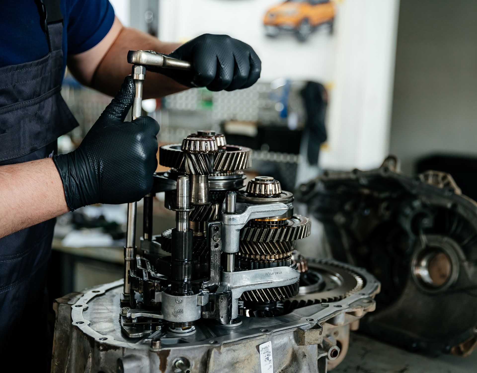 Mechanic in black gloves working on exposed car transmission gears in a workshop