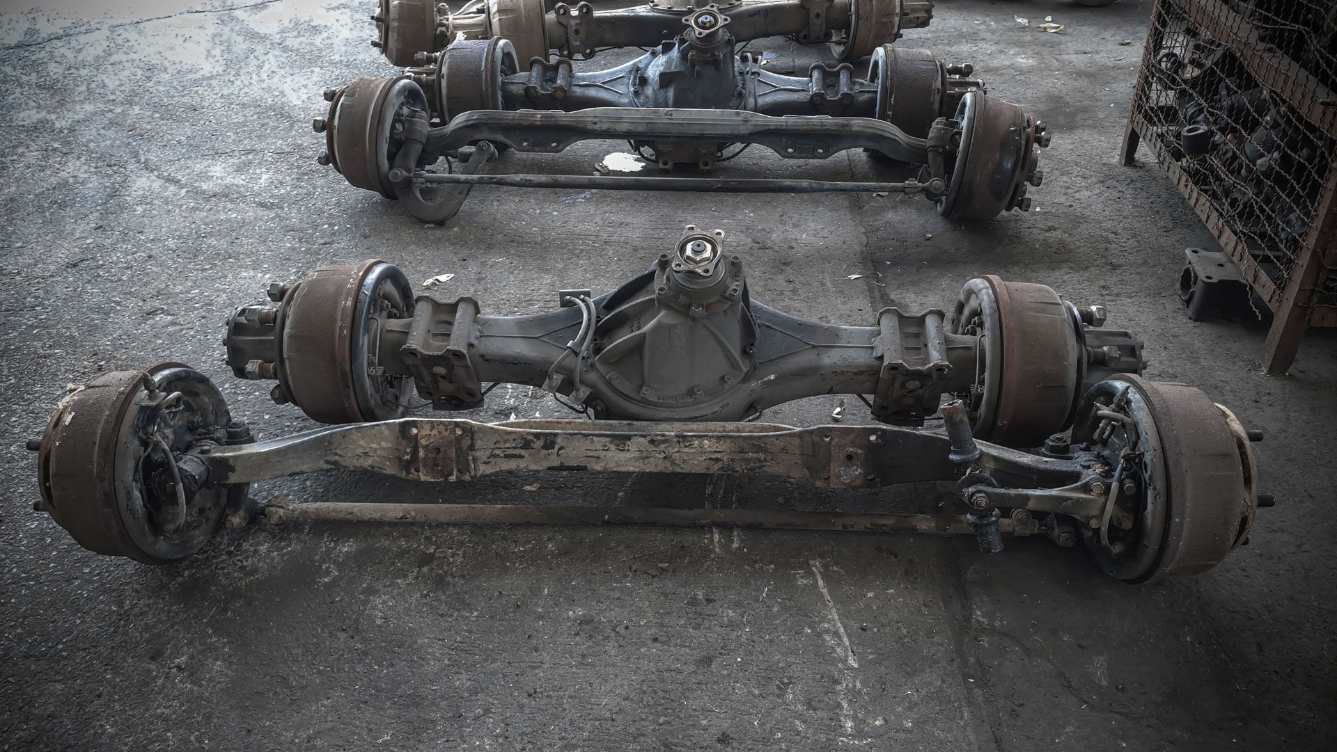 Two rusty vehicle axles with wheels lying on a wet concrete floor in a workshop