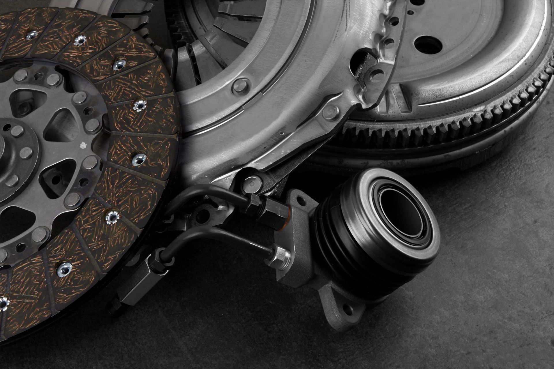 Automotive clutch and flywheel parts, including a worn disc, arranged on a dark surface