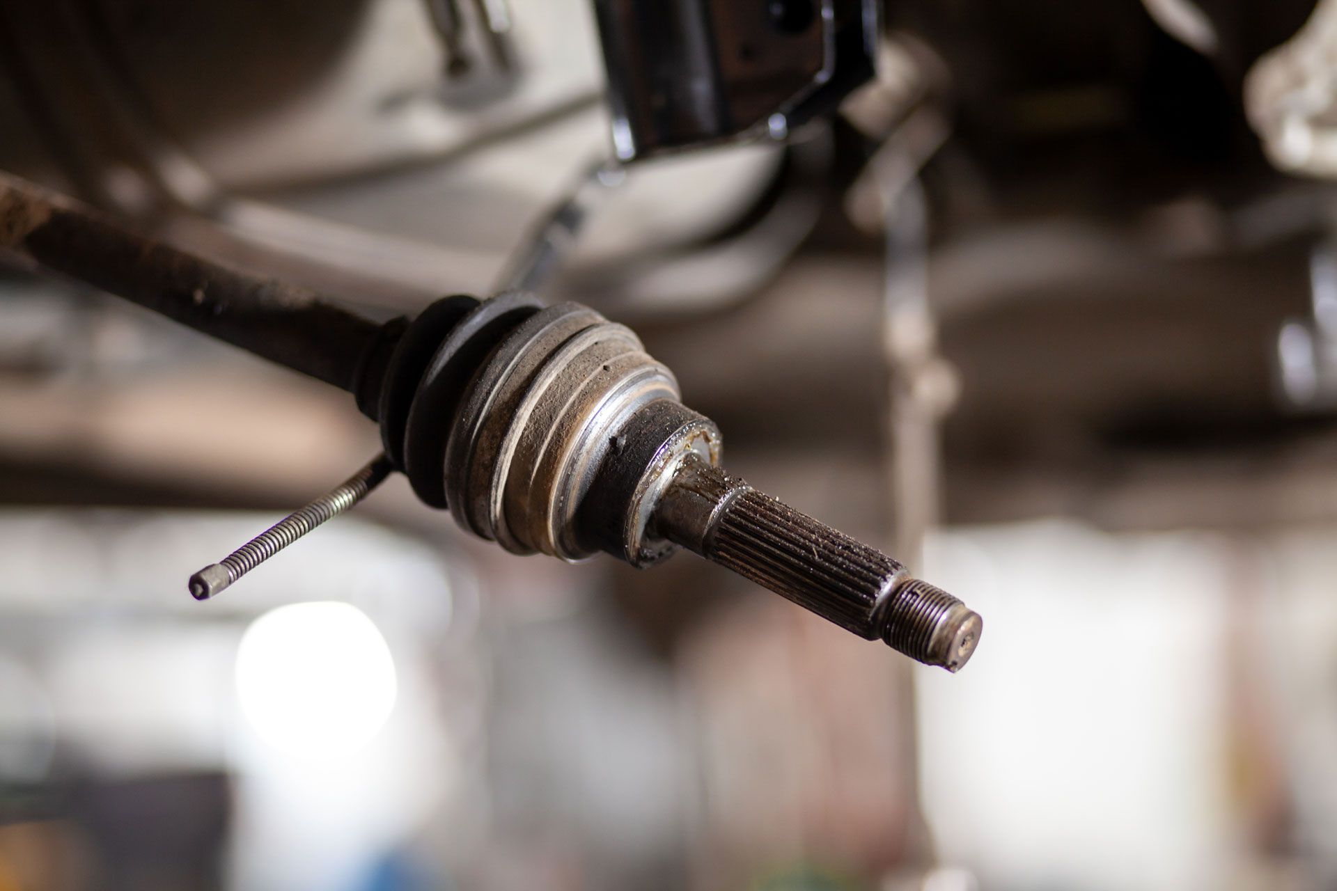Close-up of a car CV axle and rubber boot in a garage, with the shaft extending toward the camera