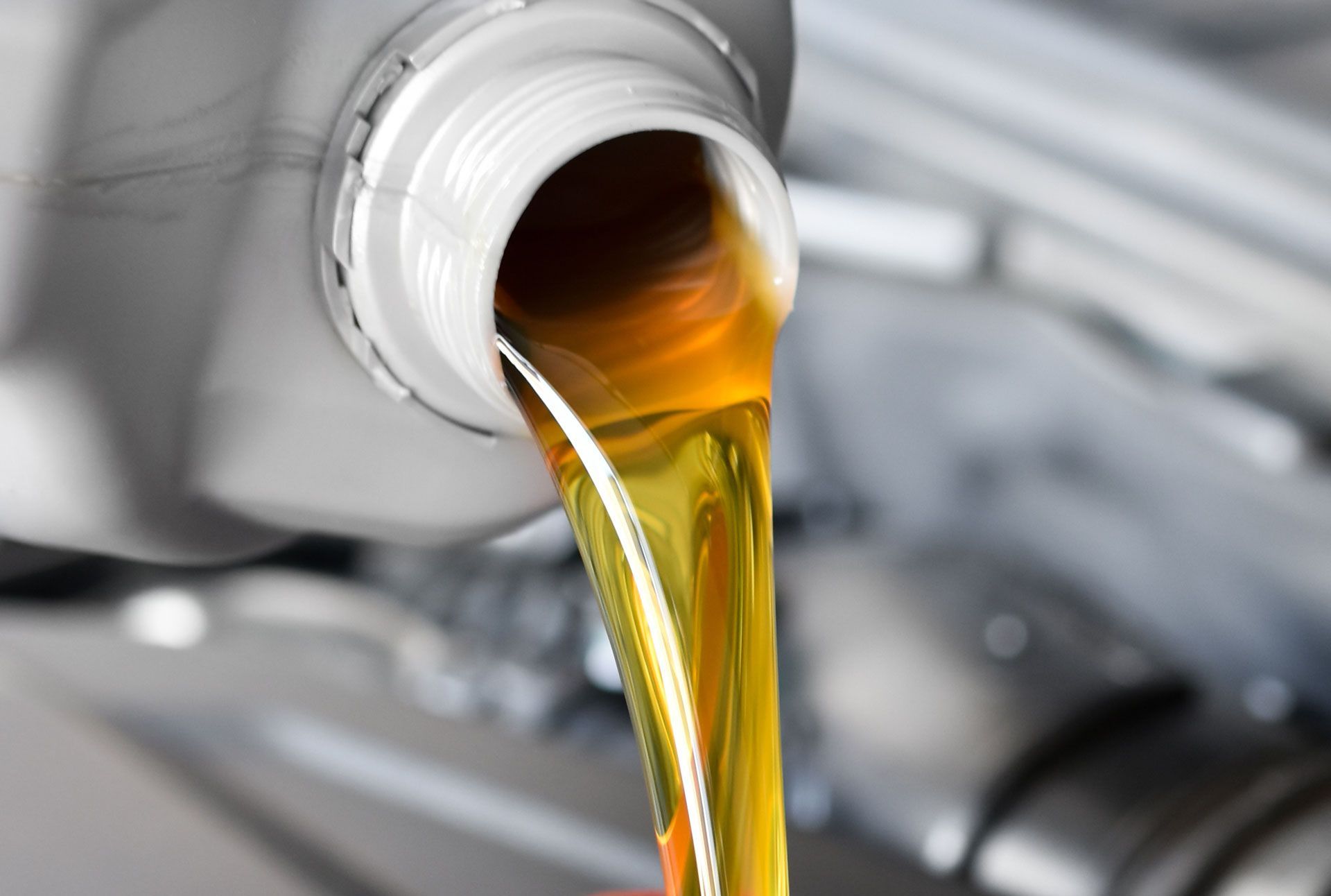 Golden motor oil pouring from a white bottle into an engine